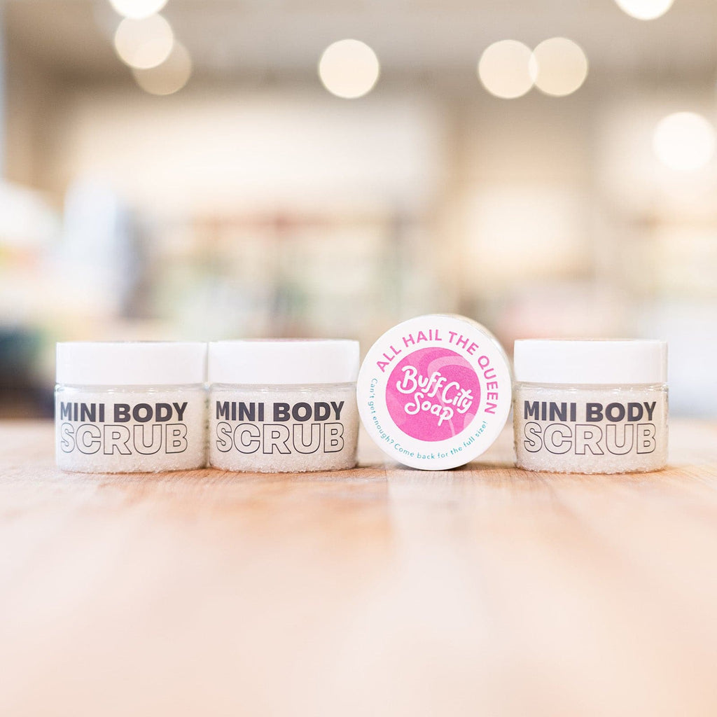 Four clear Mini Body Scrub containers with white and pink lids lined up on counter