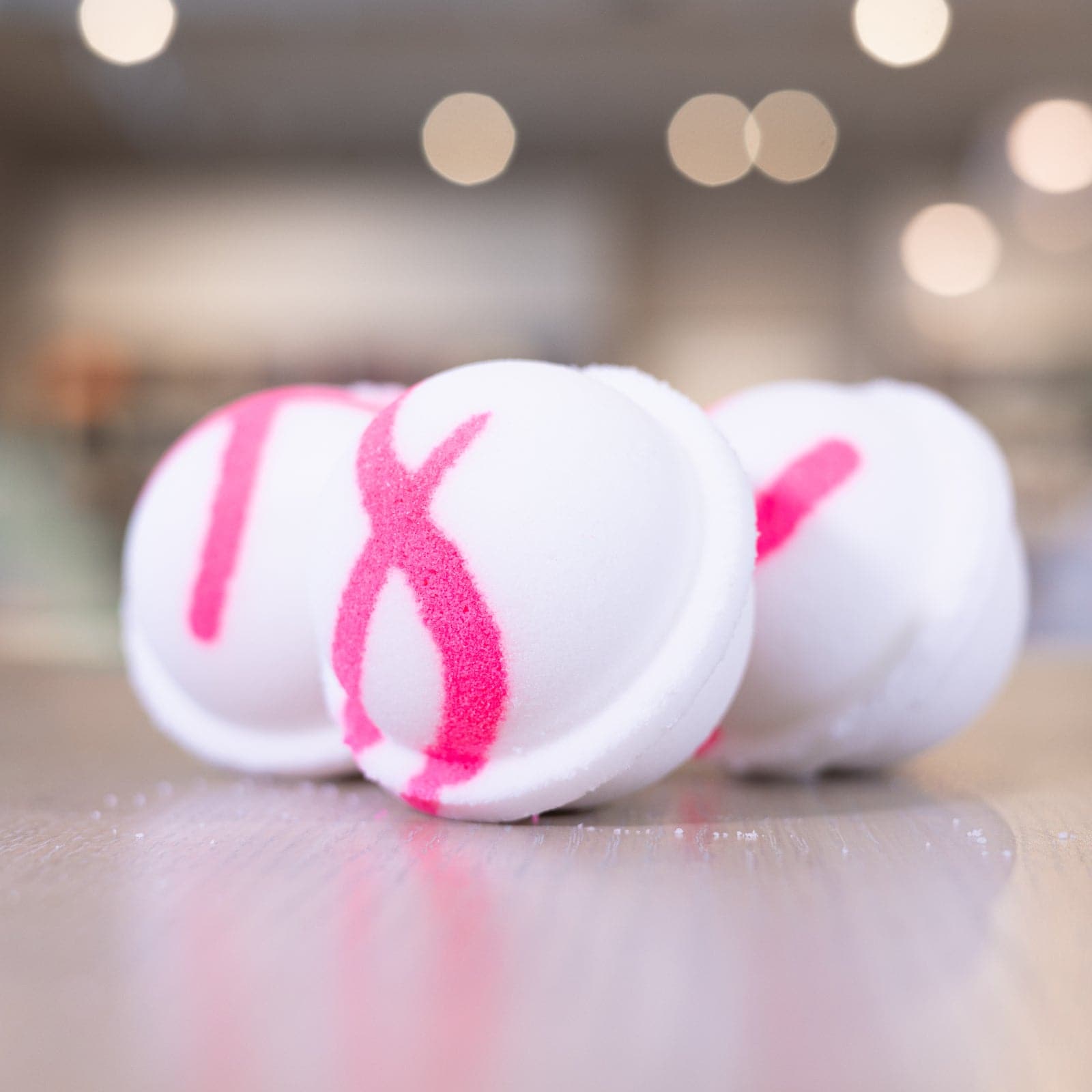 Three white bath bombs with pink design staggered on counter