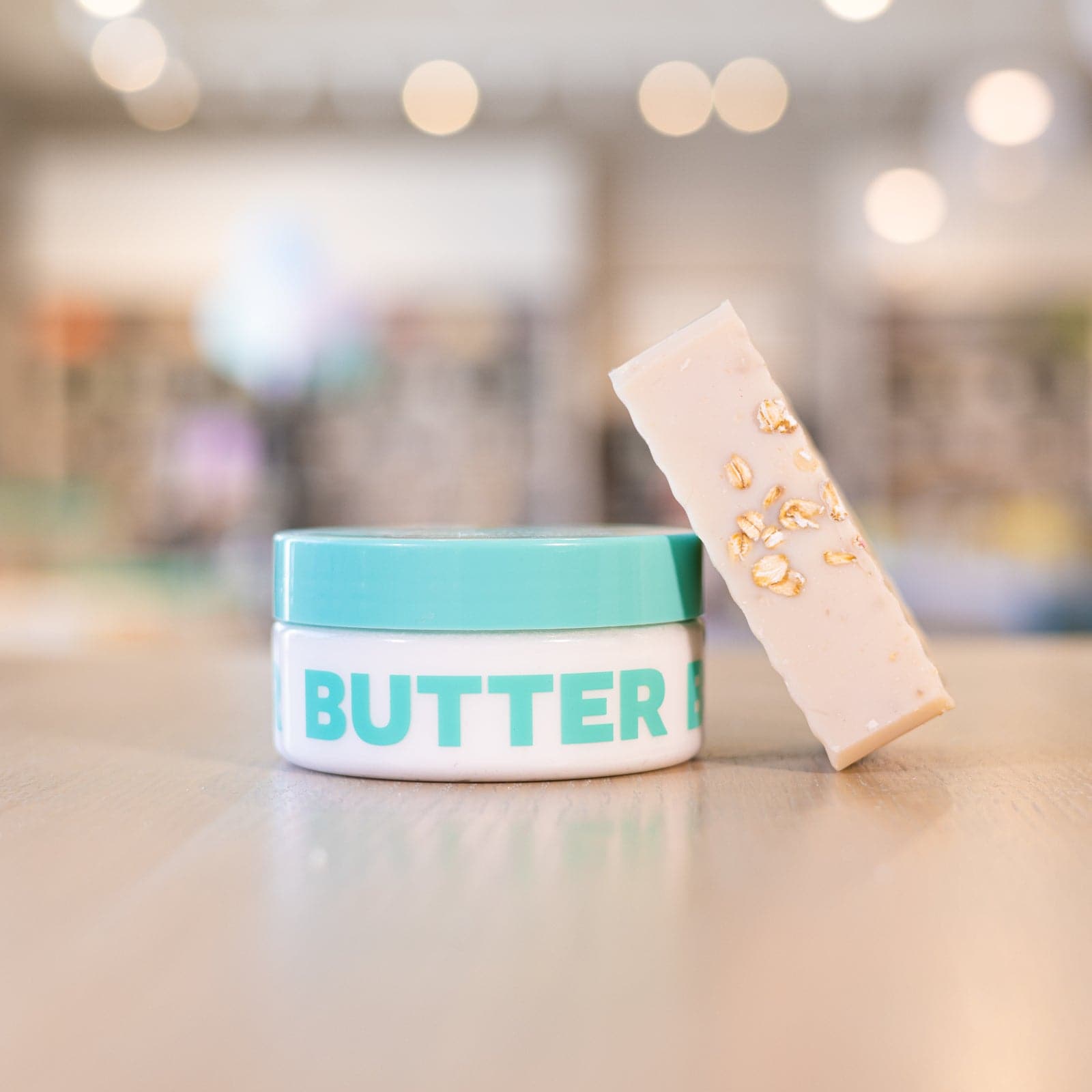 Tan soap bar with oats inside leaning against Body Butter on counter